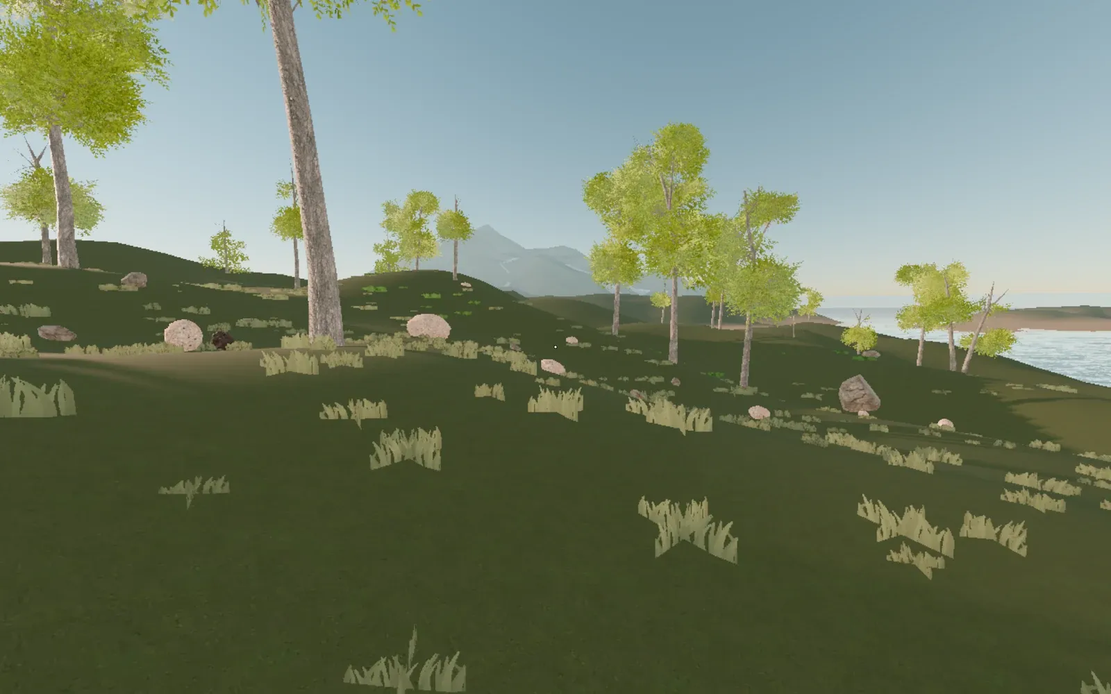 Grassland with young trees and boulders, rolling down to a lake under distant mountains.